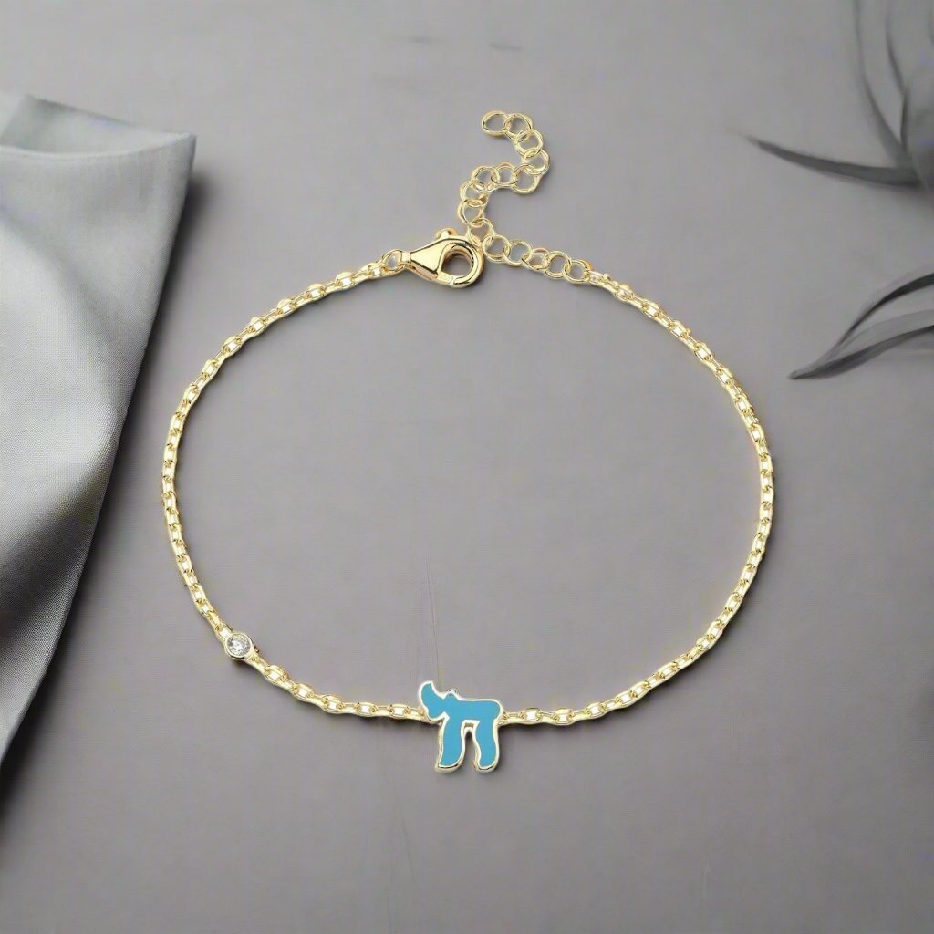 Chai Hebrew bracelet in sterling silver or 14k gold, featuring a pink or blue gemstone, symbolizing life and faith.
