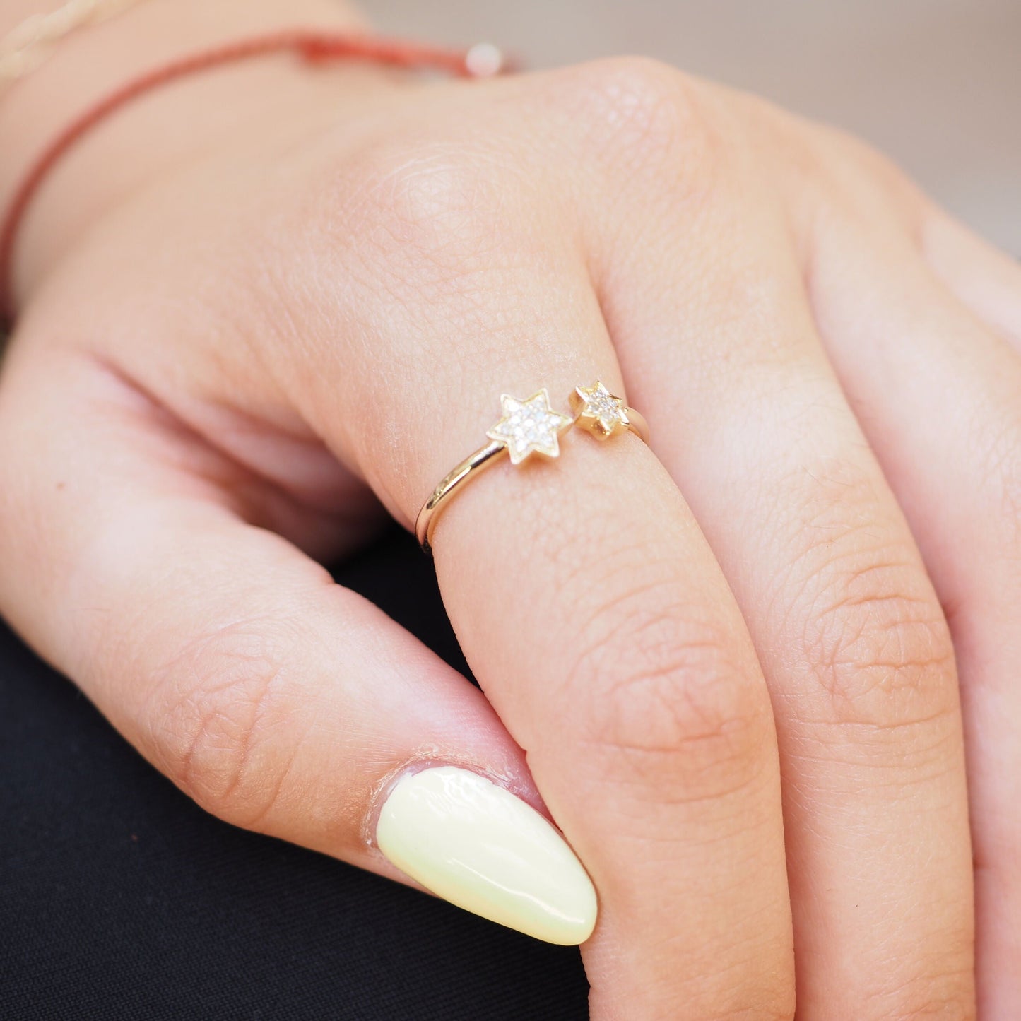 A close-up of a hand wearing a delicate gold ring with two small star-shaped charms, one clear and one gold, resting on a dark surface.