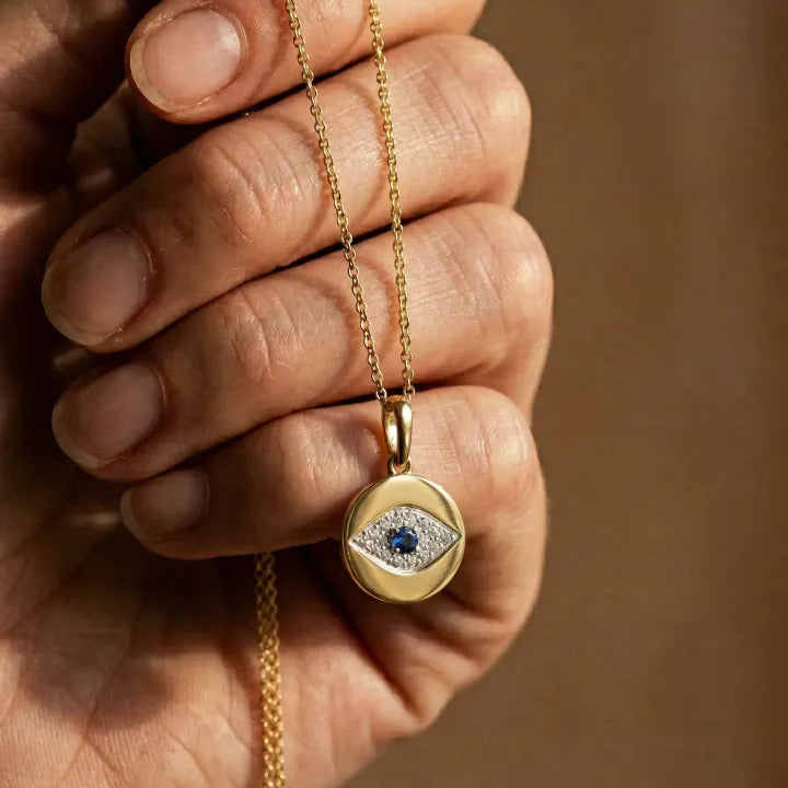 Gold necklace with an eye-shaped pendant held in a hand against a brown background