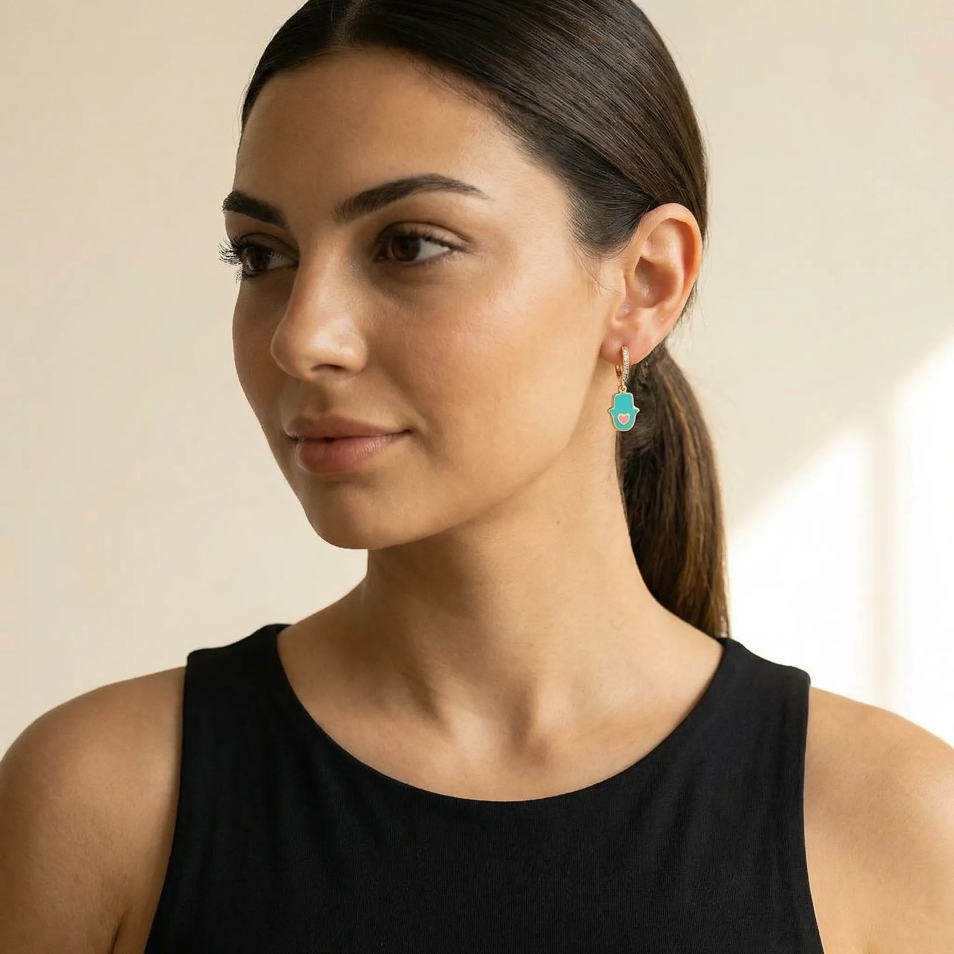 Hamsa hand huggie earrings in pink with CZ accents and high-polish finish by Alef Bet