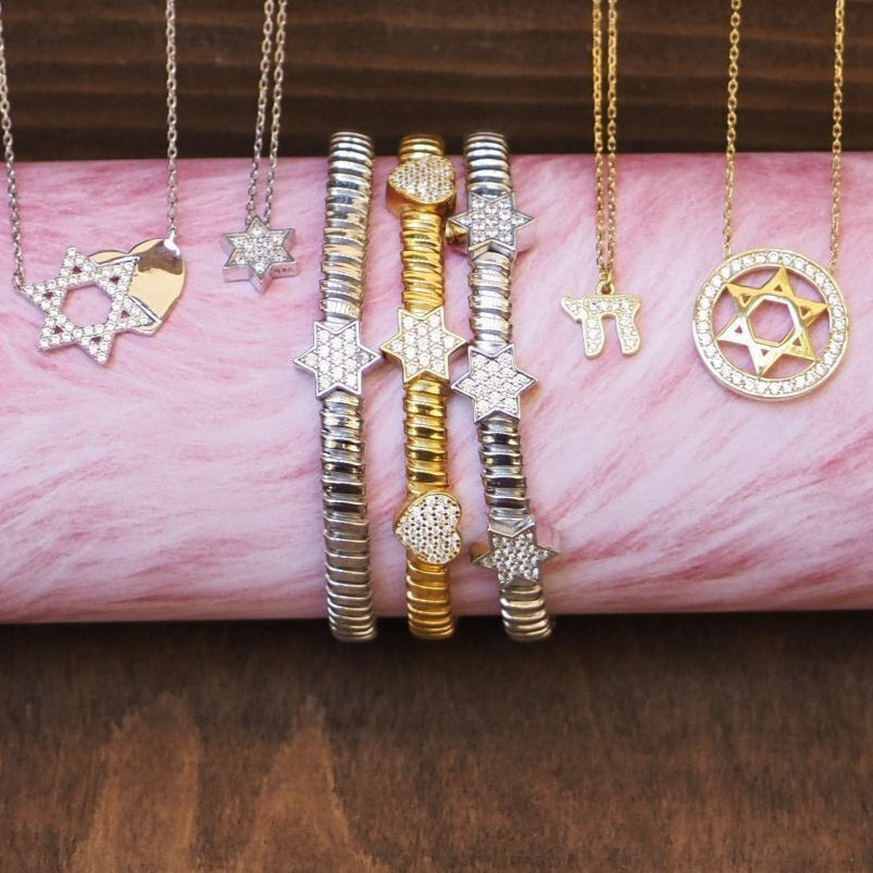 Gold and silver jewelry including necklaces and bracelets on a pink marble surface.