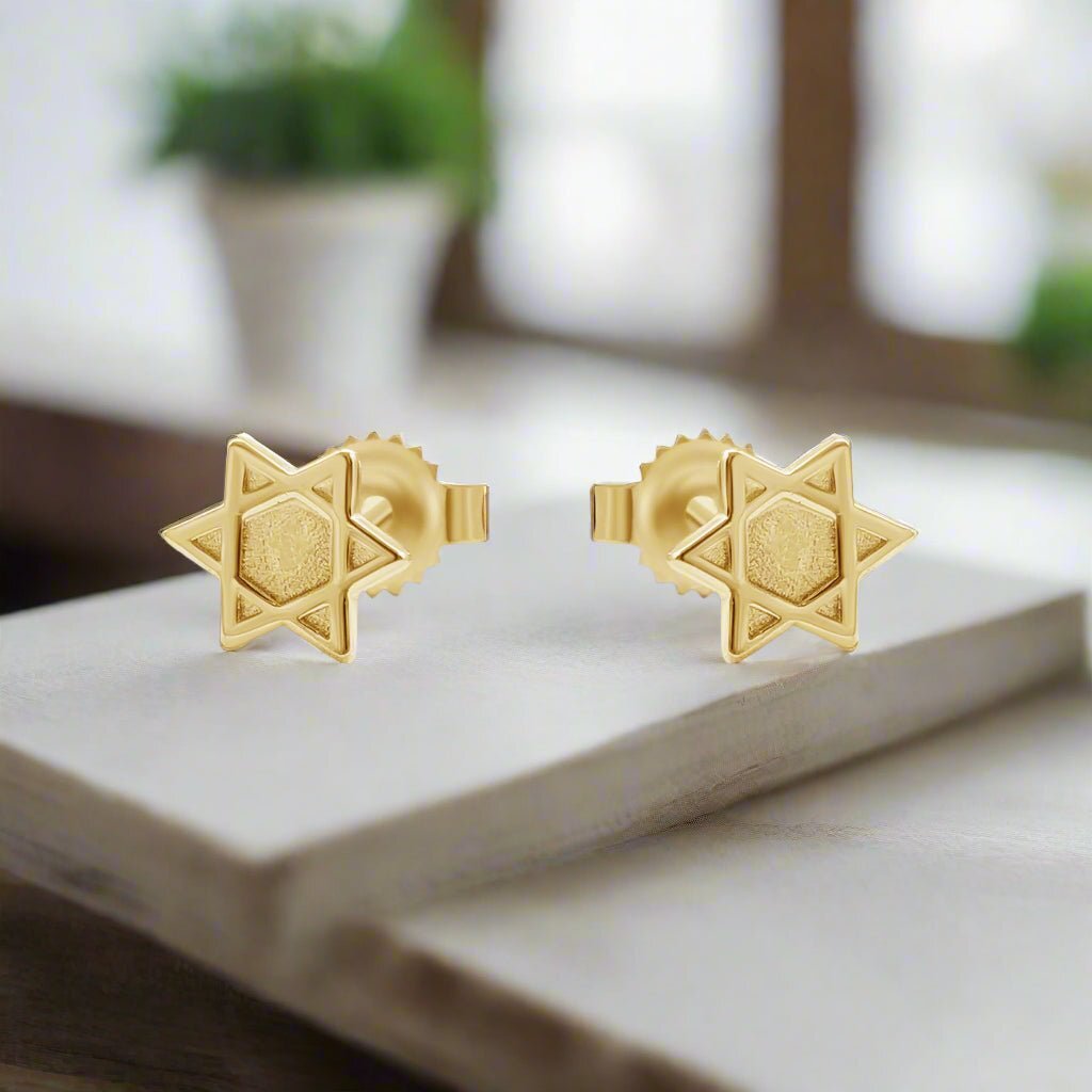 Gold star david shaped earrings on a marble surface with a blurred background