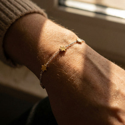 Bracelet with star charms on a wrist, sunlight casting shadows
