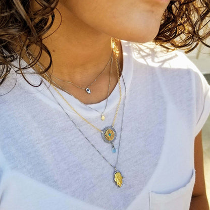 Close-up of a person wearing multiple necklaces with detailed pendants on a white shirt.