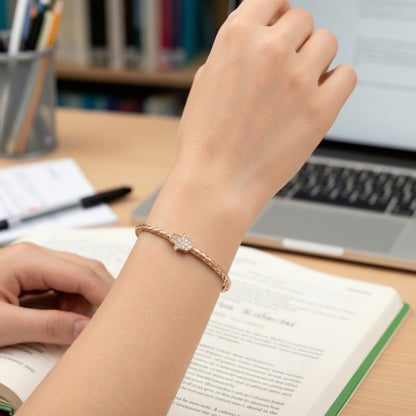 Person wearing a bracelet on a desk with books and a laptop in the background