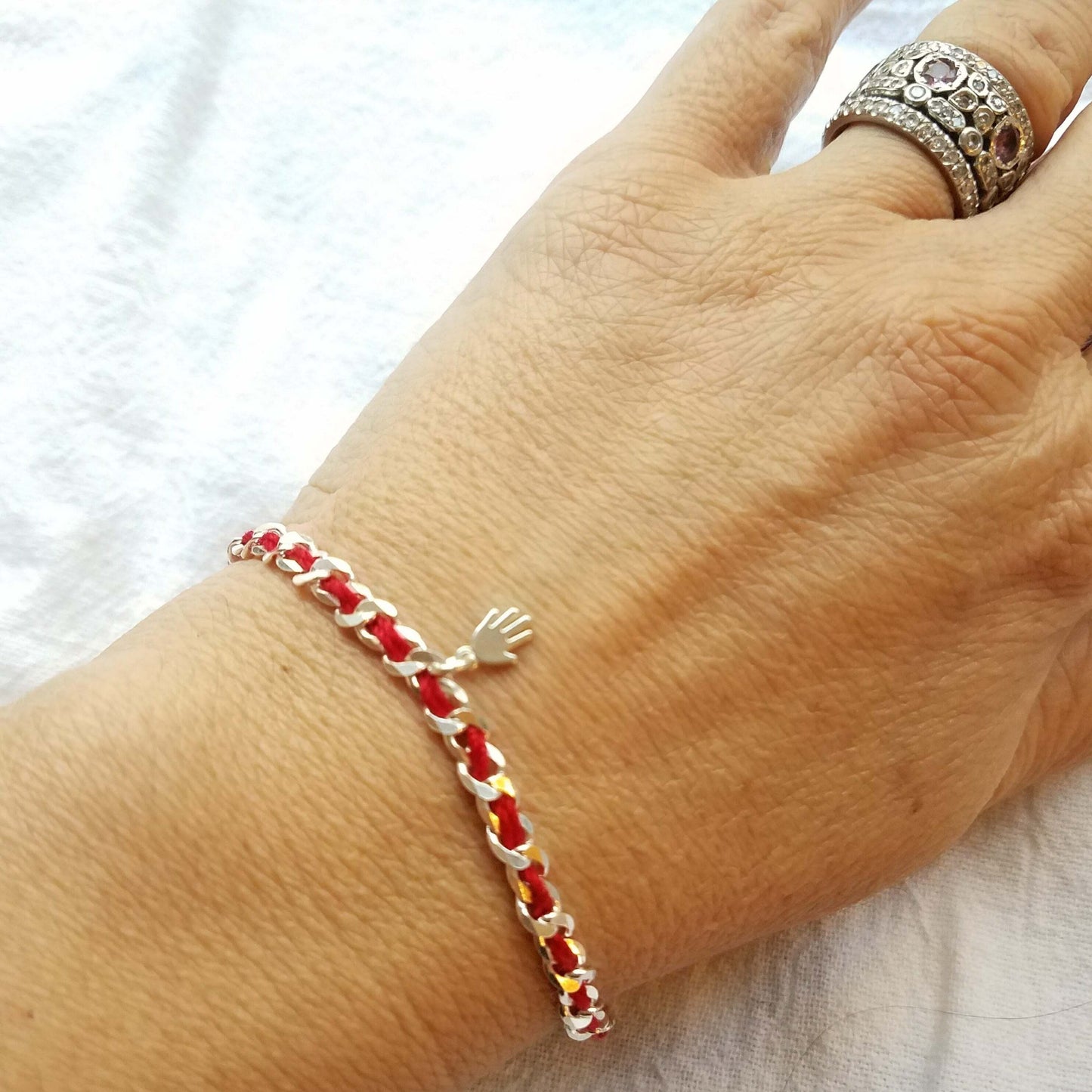Sterling silver bracelet with a hamsa charm on a red string, symbolizing protection; gift wrapped, suitable for various occasions.