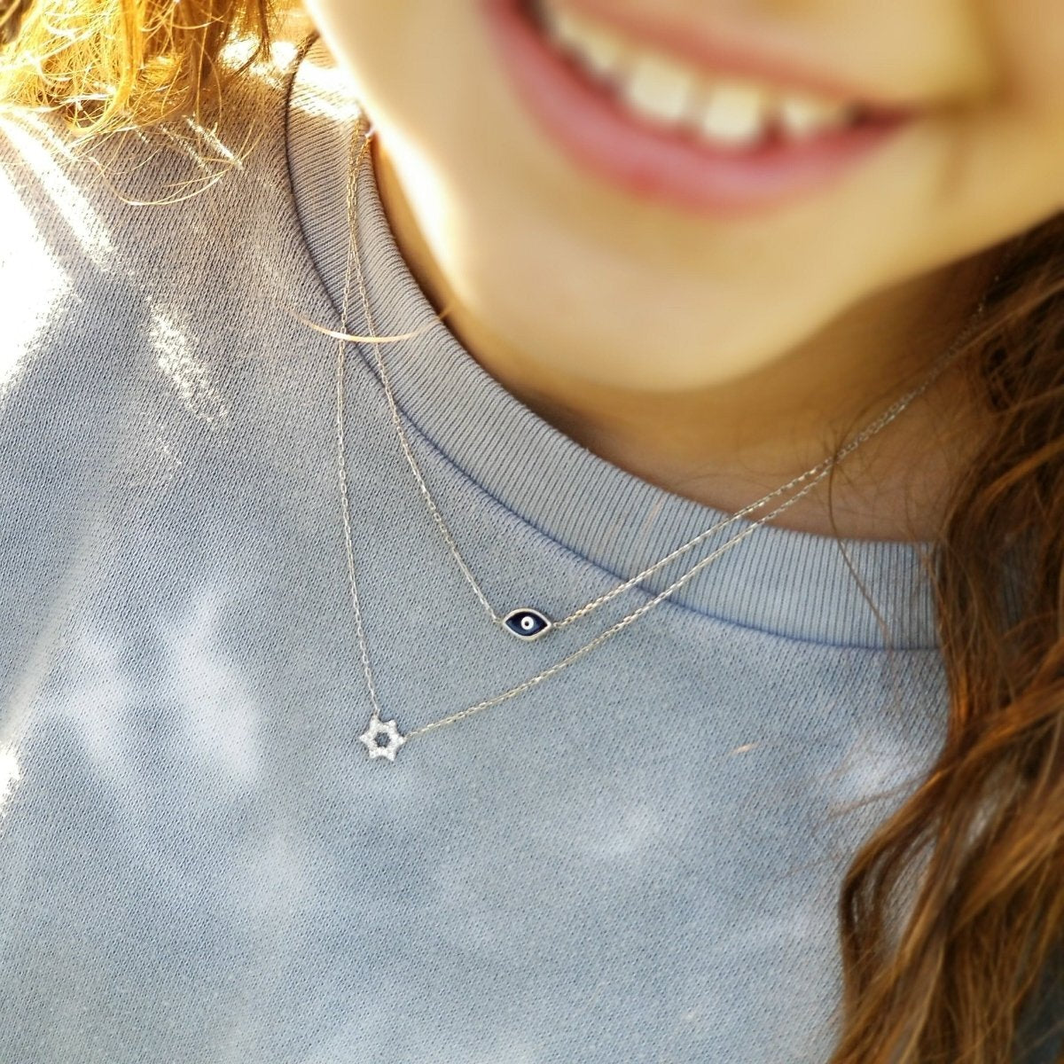Close-up of a person wearing two necklaces with star and eye pendants on a light blue shirt.