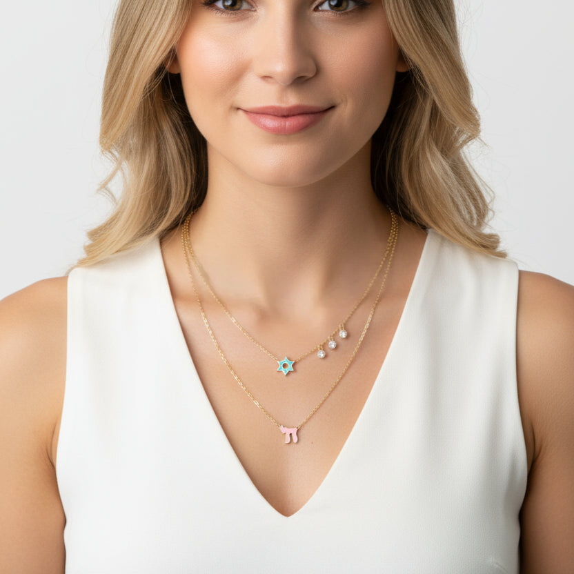 Two chains with a clasp feature a pink enamel Chai and Star of David charms, adorned with glistening gems for a timeless look.