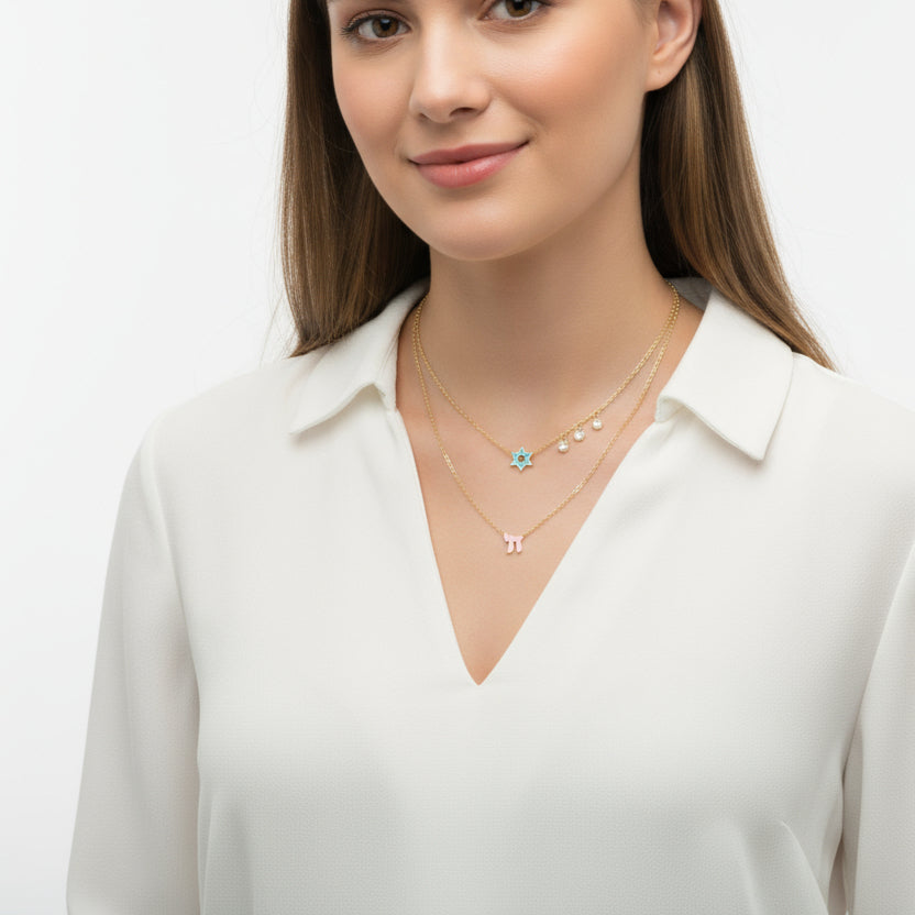A layered necklace featuring a pink Star of David and Chai charms, accented with diamond-like gems for a timeless look.