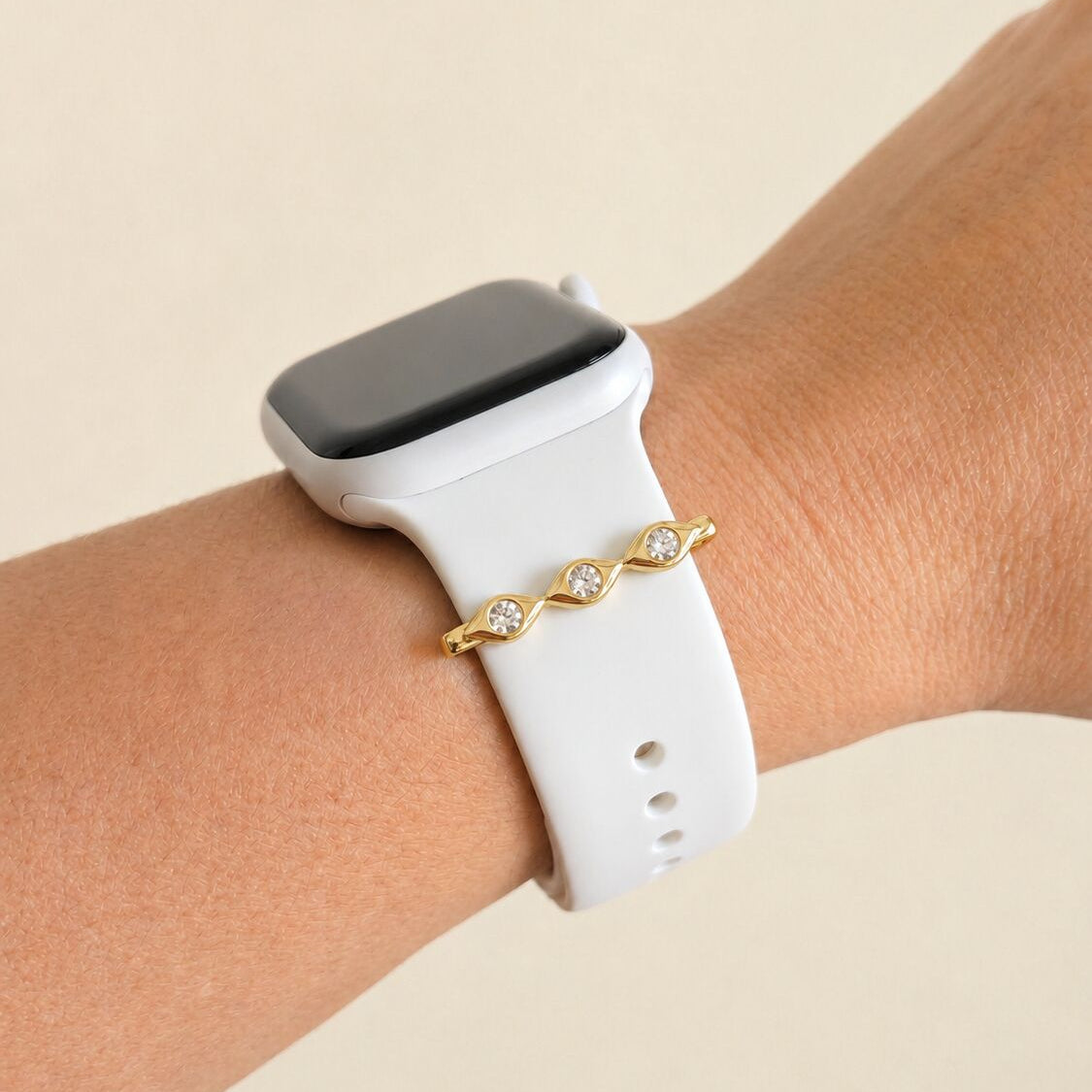 Smartwatch with a white band on a wrist, wearing a evil eye gold charm against a beige background