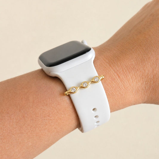 Smartwatch with a white band on a wrist, wearing a evil eye gold charm against a beige background