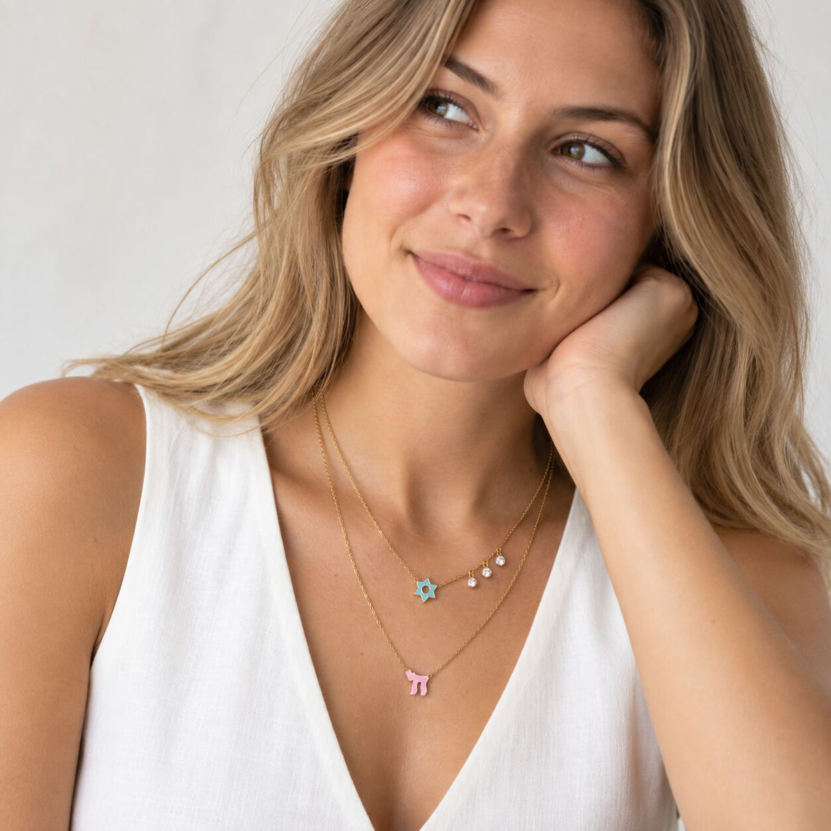 A layered necklace featuring a pink Star of David and Chai charms, accented with diamond-like gems for a timeless look.