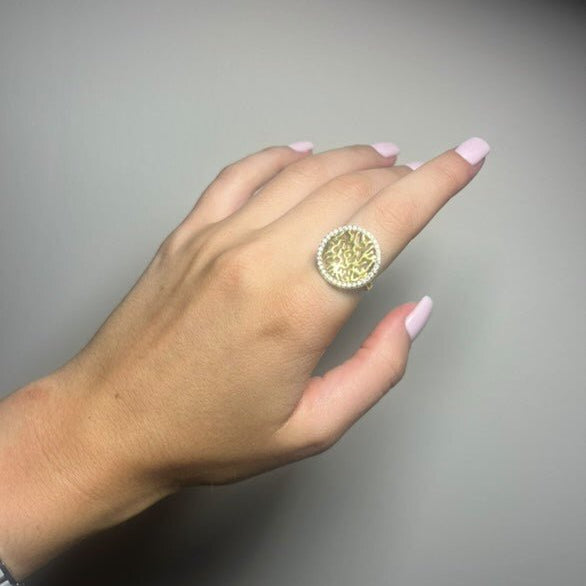 Hand wearing a gold ring with a textured design on a gray background