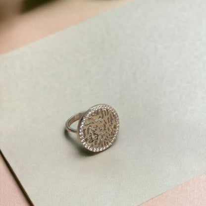 Silver ring with intricate design on a light green card