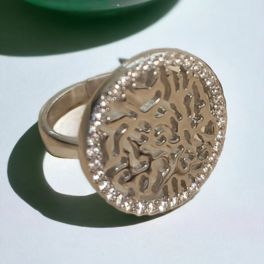 Gold ring with intricate design on a light blue surface